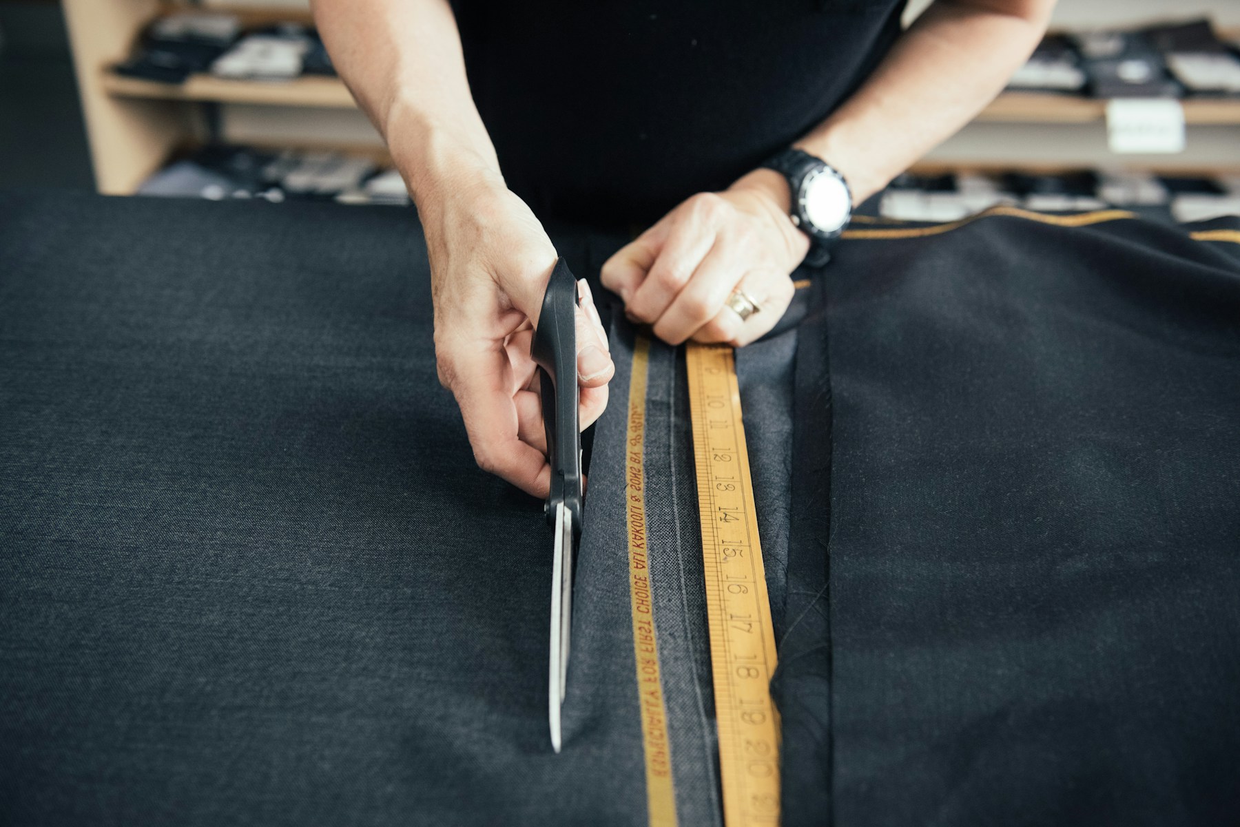 A tailor carefully cutting dark cloth with shears and a measuring rule