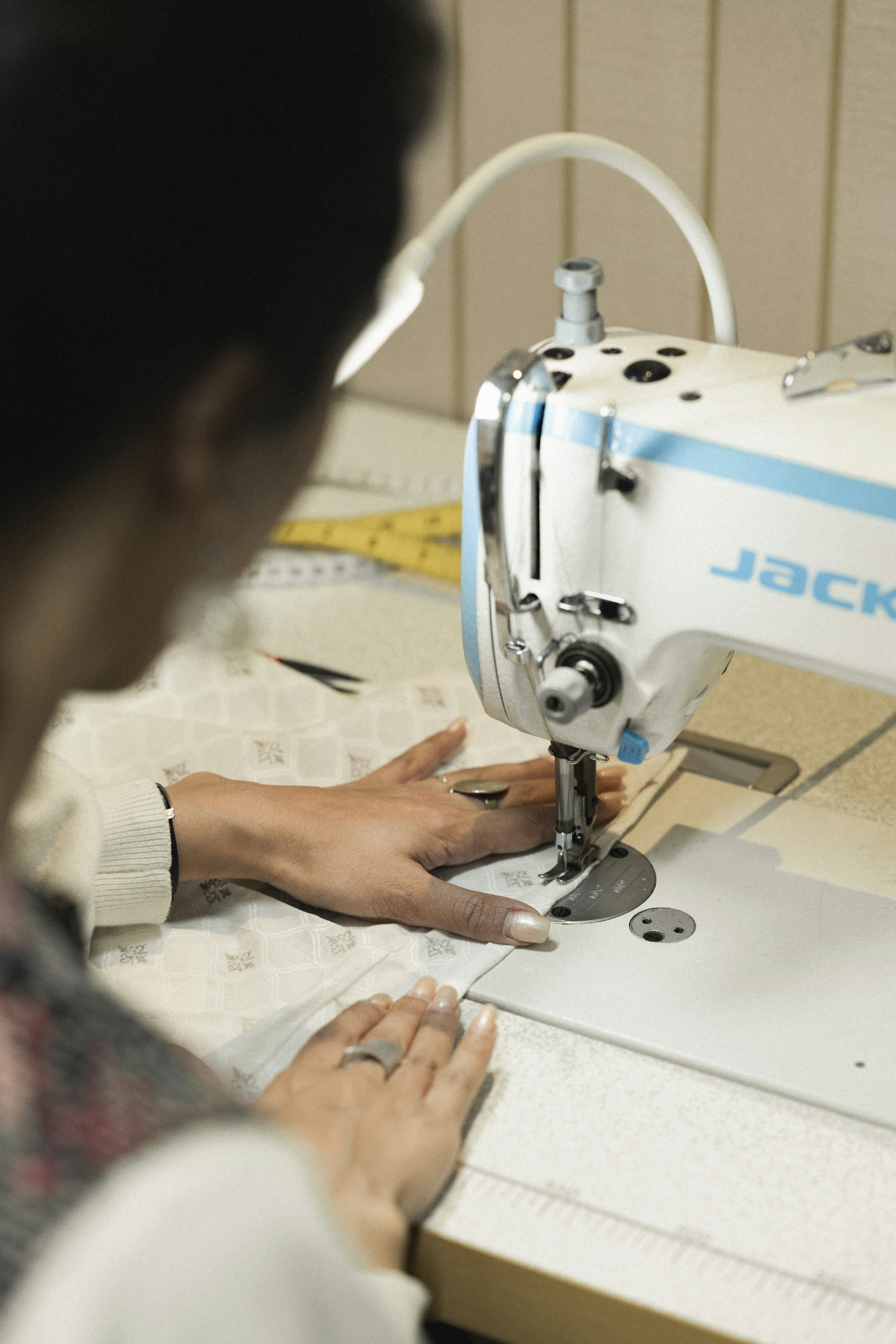 A garment maker carefully stitching pale fabric at a sewing machine